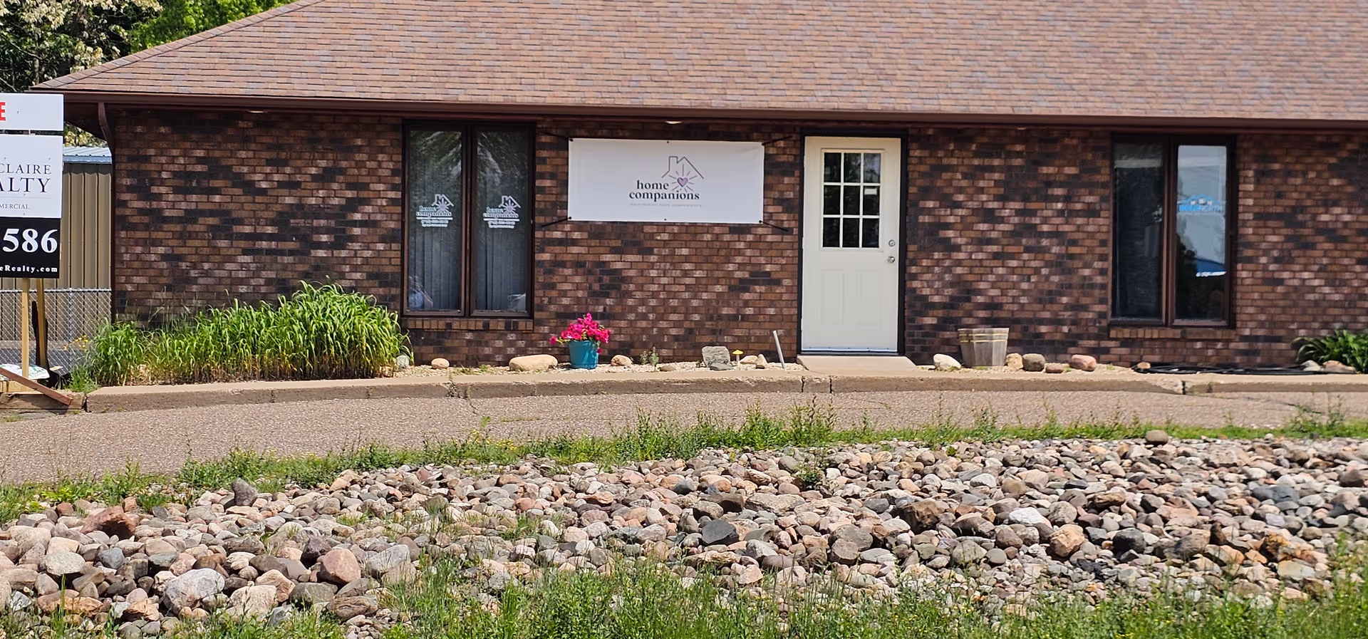 Brick building front with Home Companions banner, entrance door, and rocky landscaping.