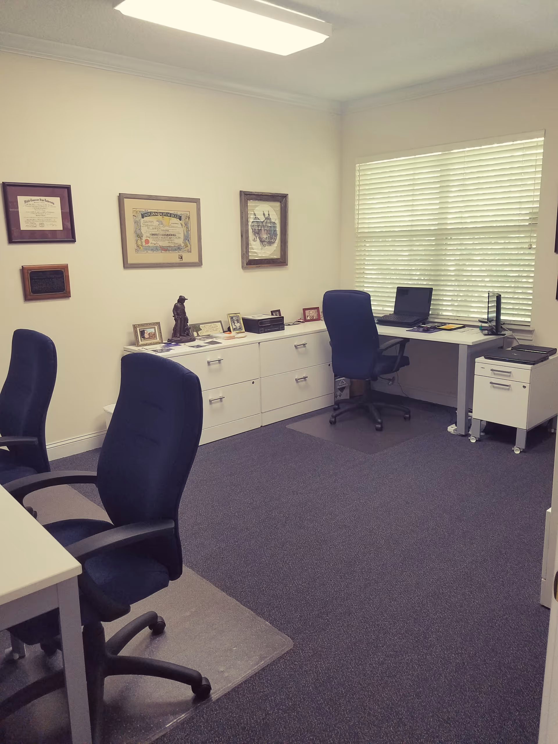 A senior living facility office with blue chairs, desks, and framed certificates.