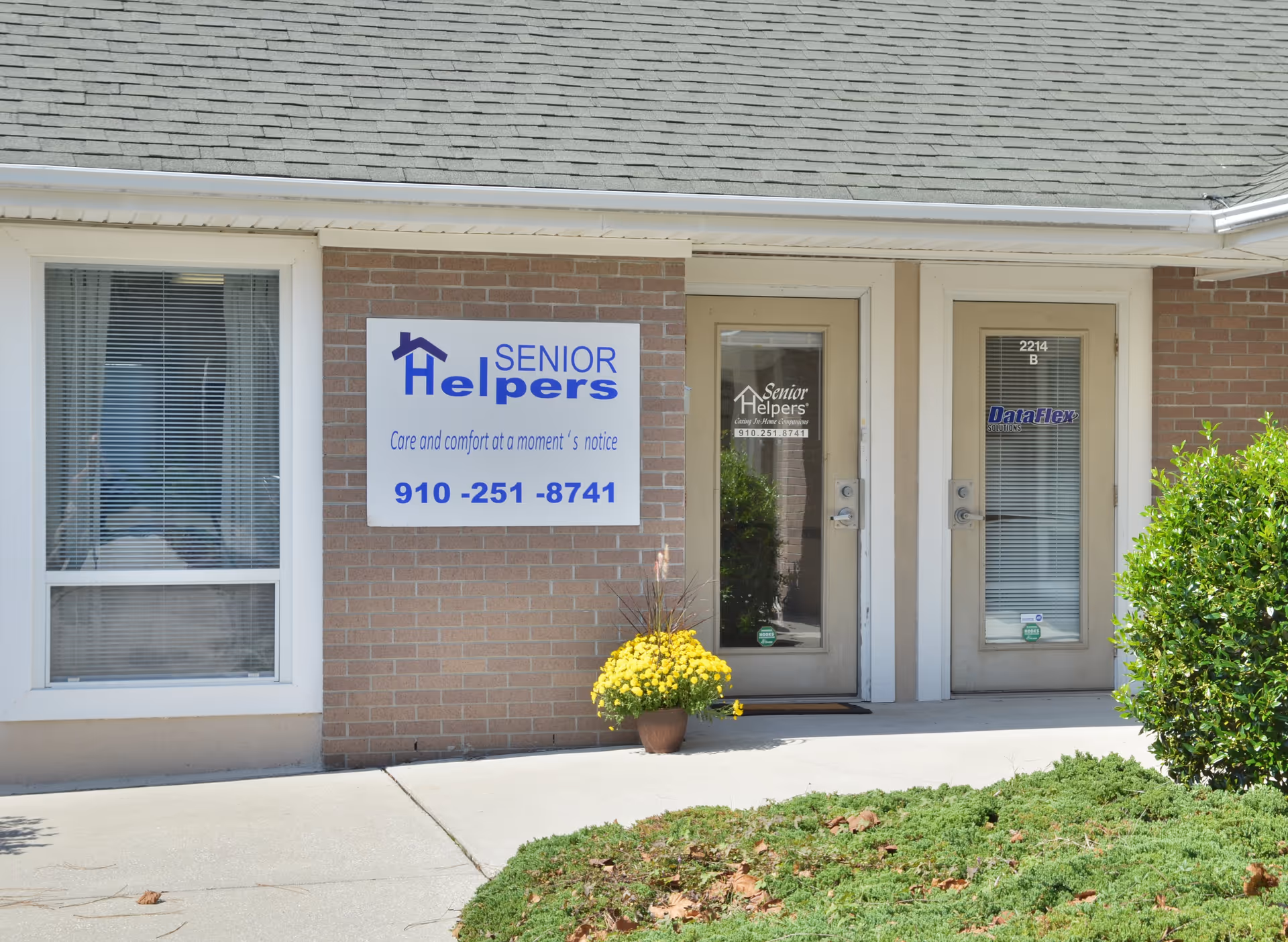 Exterior view of a Senior Helpers facility with a sign, glass doors, window, and a potted plant.