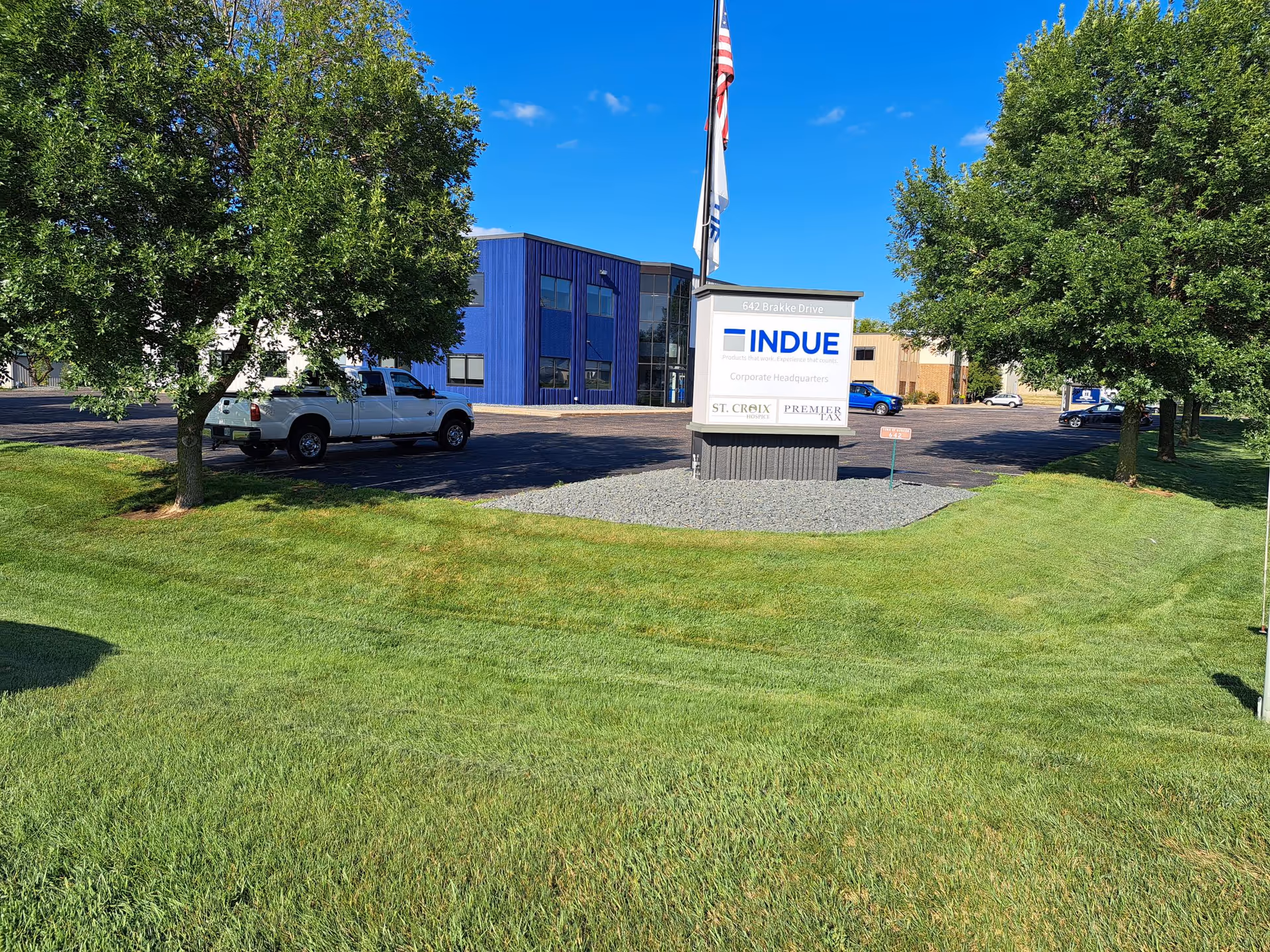 Exterior view of a blue corporate building with a sign and flag, surrounded by green lawn.