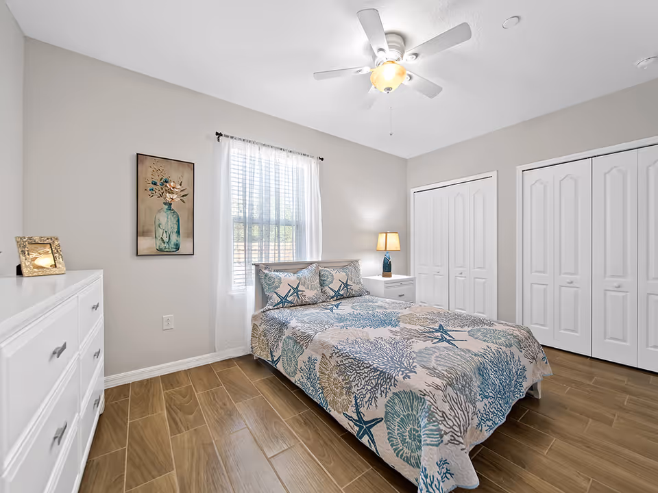 Bright bedroom with a bed, dresser, and white closet doors.