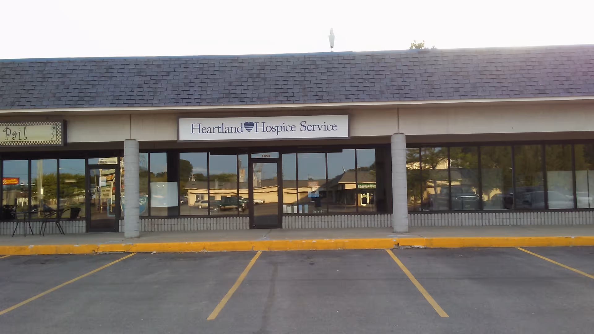 Exterior of a strip mall with a Heartland Hospice Service storefront and glass doors.