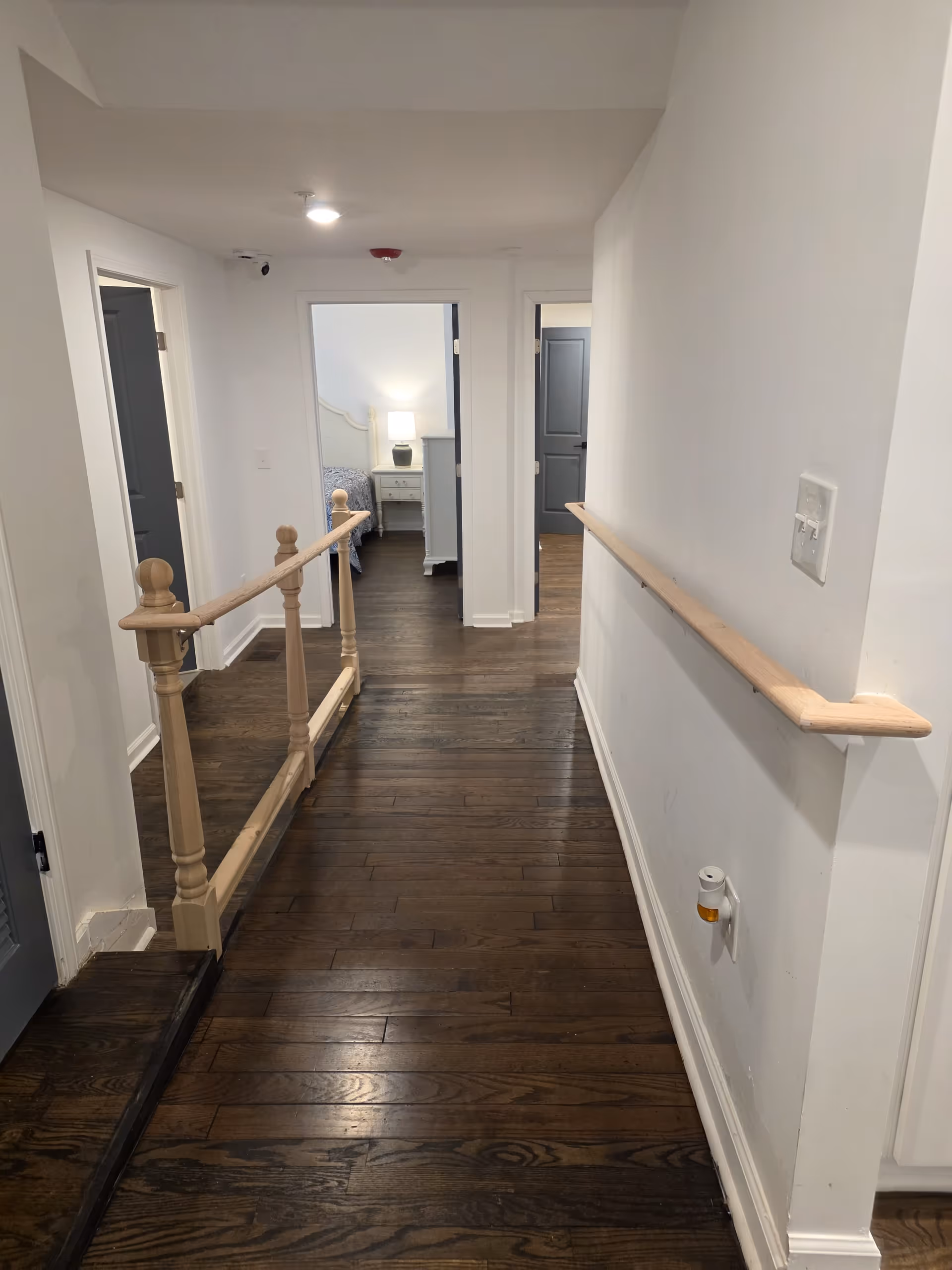 Hallway inside a senior living facility with wooden floor, railing, and doors to rooms