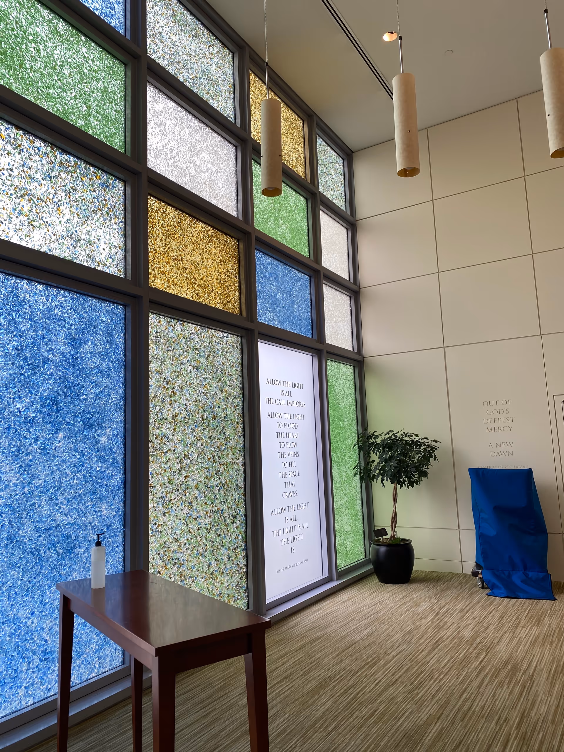 Bright interior lobby with colorful stained-glass windows, a small table, plant, and blue chair cover.