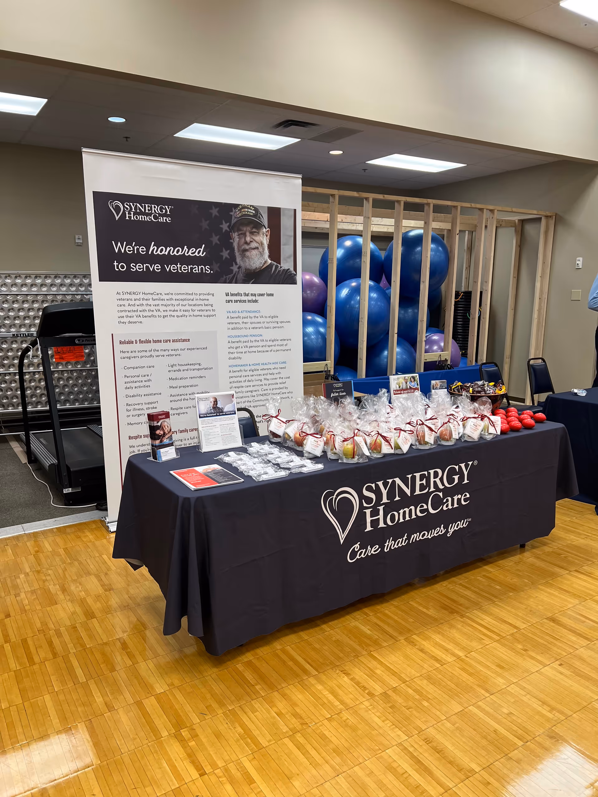 Synergy HomeCare information table with a banner, giveaway items, and blue exercise balls indoors.