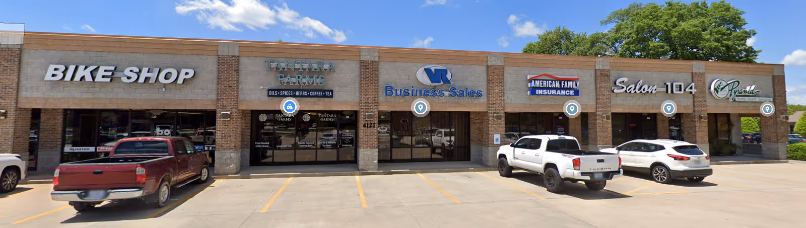 A strip mall exterior with multiple storefronts and parked cars in front.