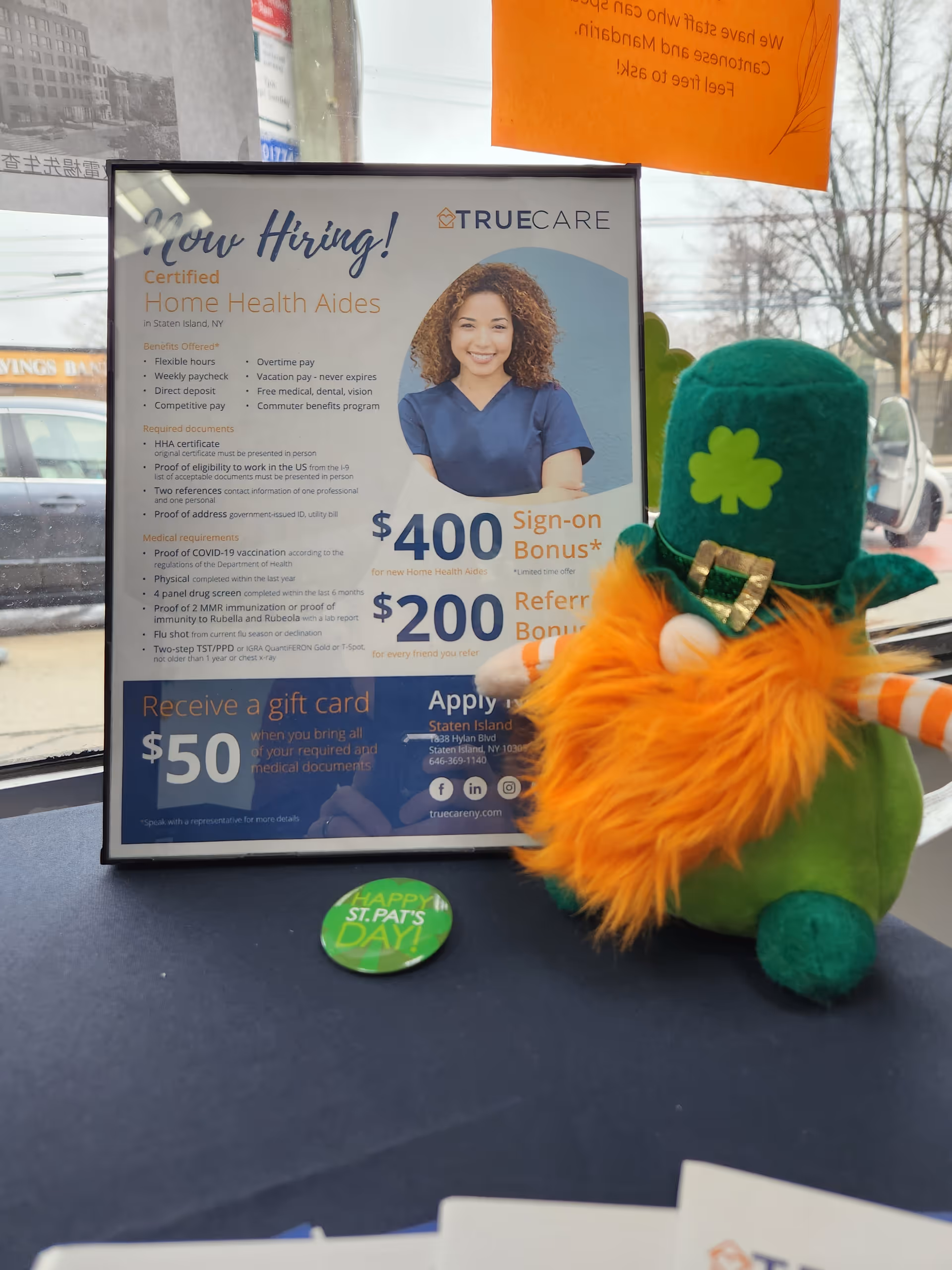 Framed TrueCare job poster on a table with a green plush leprechaun.