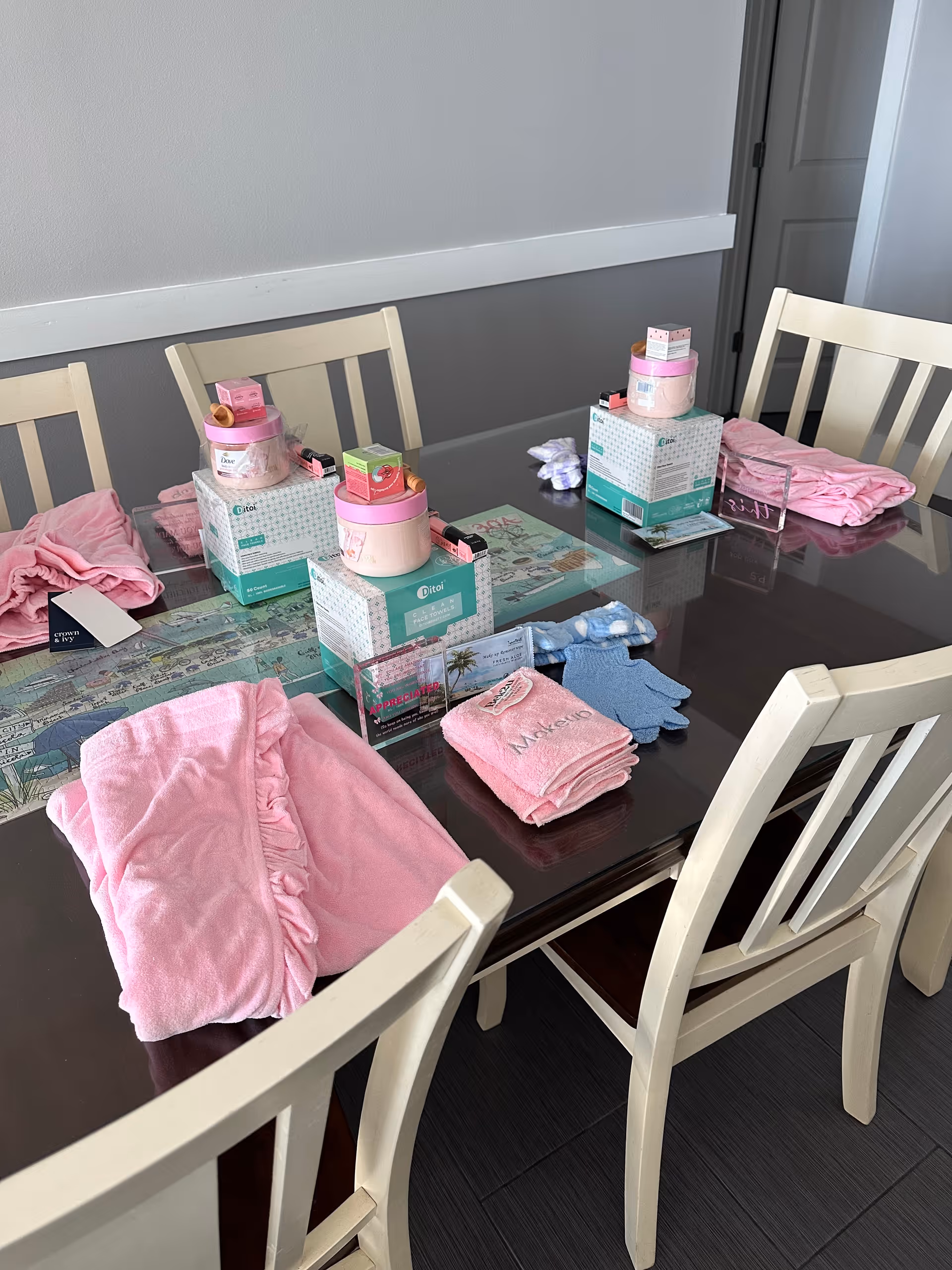A glass dining table with pink towels, care packages, and boxes in a light dining room.