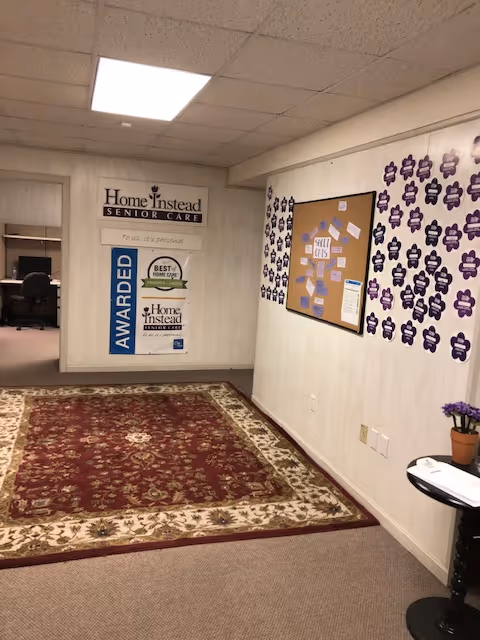 Hallway interior of Home Instead Senior Care with awards board, burgundy carpet, and purple wall decorations.