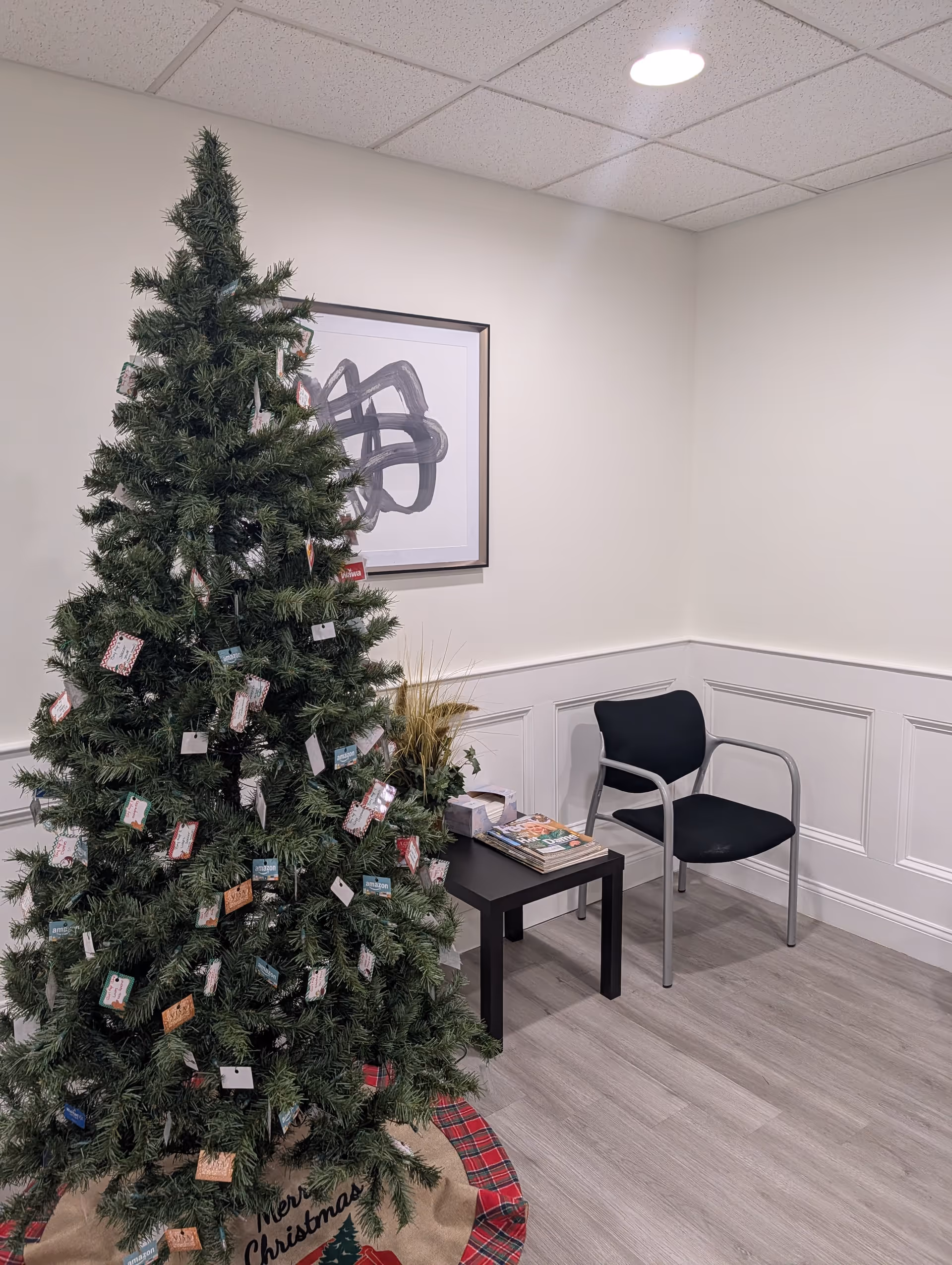 Corner of a waiting area with a Christmas tree, a black chair, and magazines.