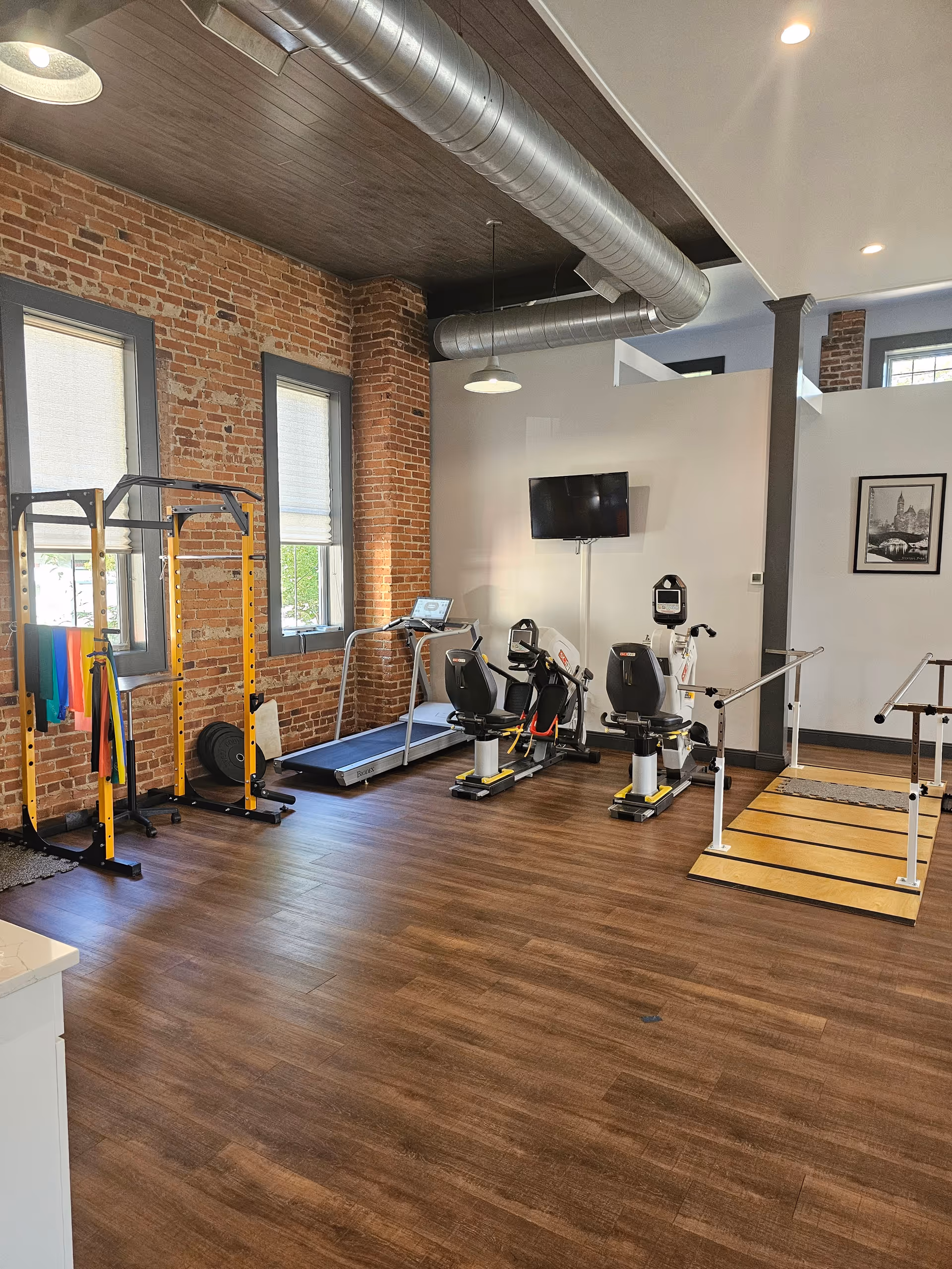 Interior fitness room at JAG Physical Therapy with brick walls, treadmills, bikes, and weight machines.