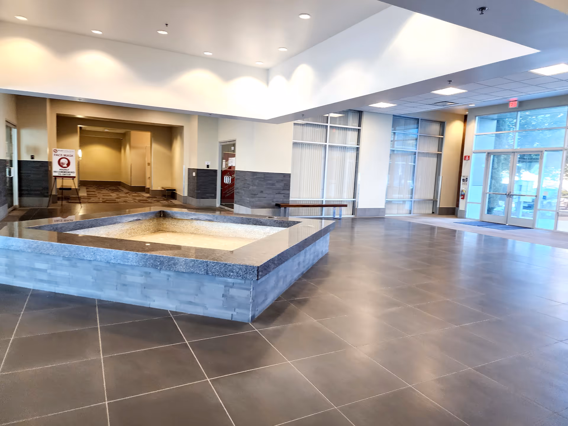 A spacious modern lobby featuring a central square sunken area and glass doors.