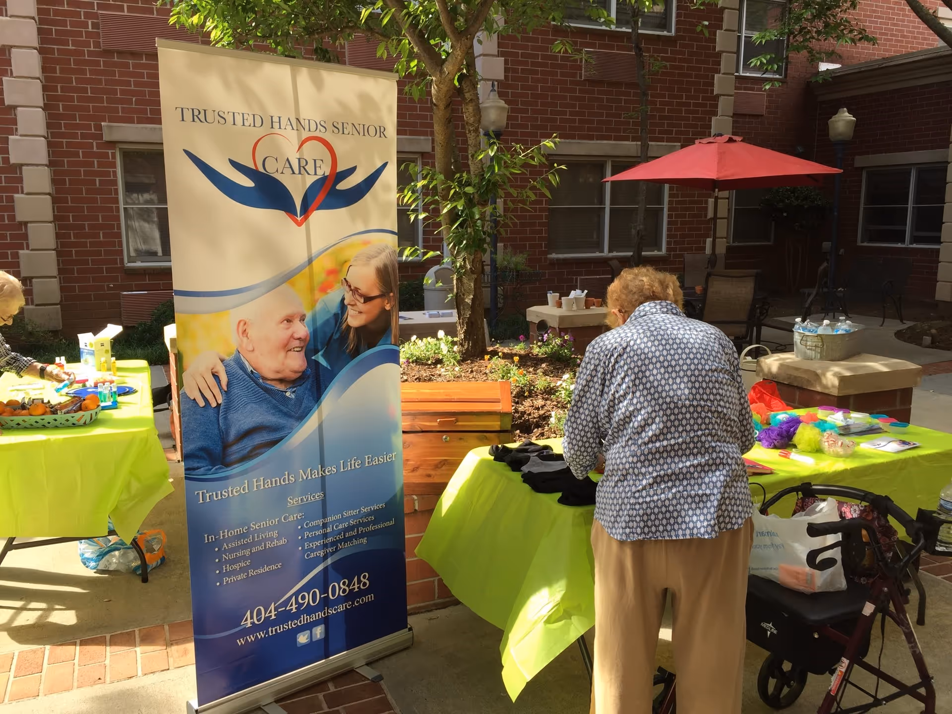 Outdoor courtyard with a Trusted Hands banner, tables, and people at an event.