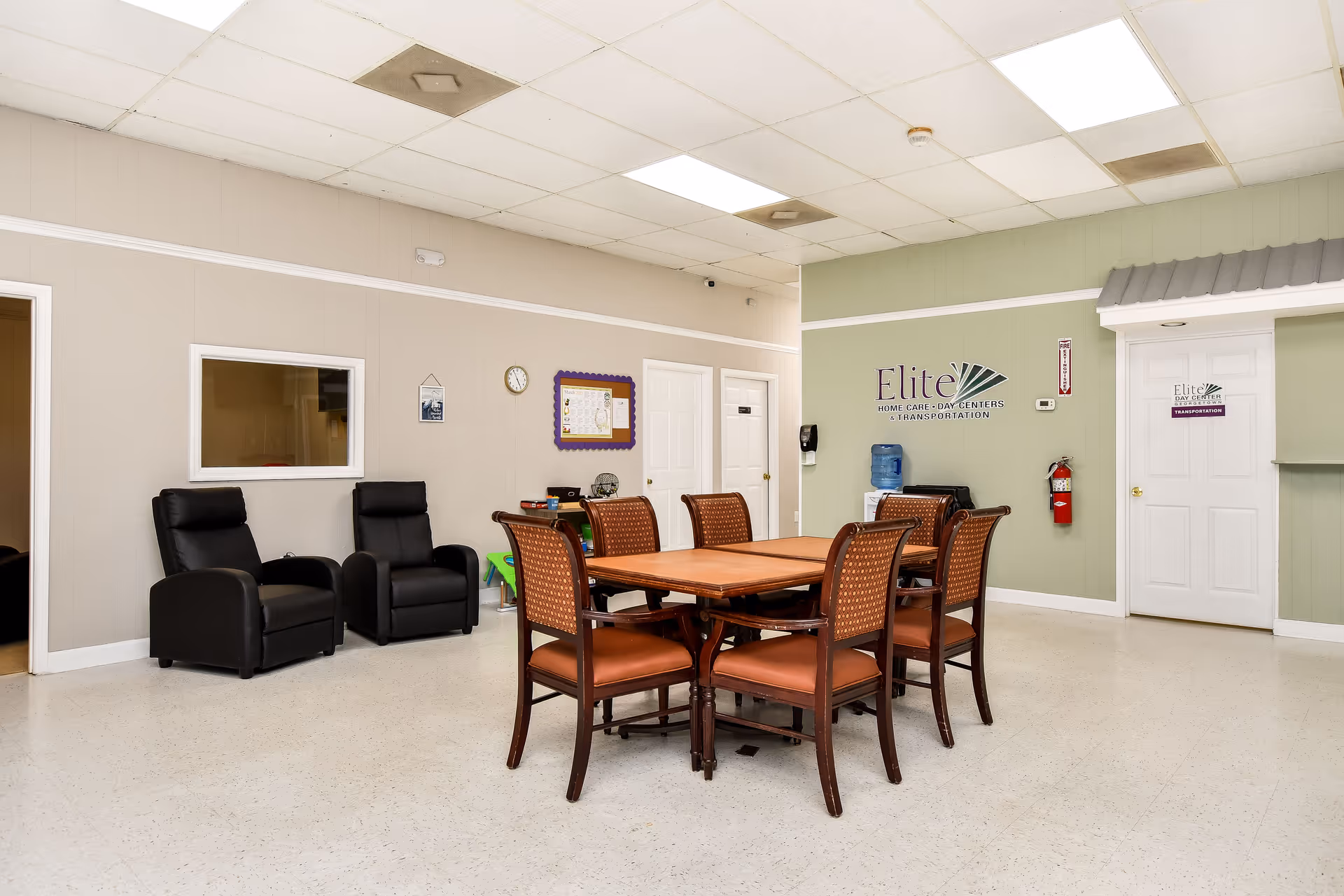 A communal dining area with a wooden table, chairs, and lounge seating in a senior facility.