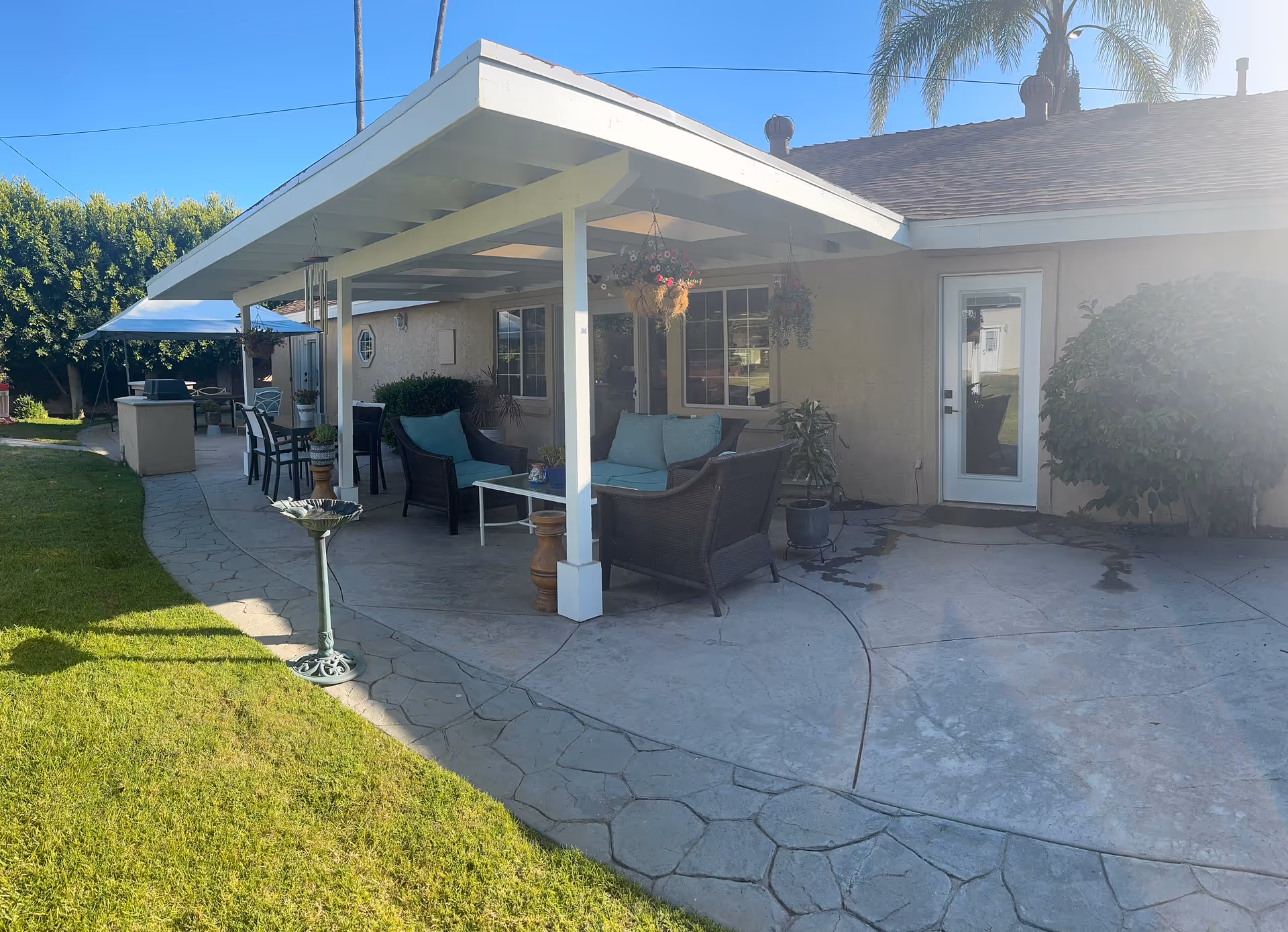 Patio seating under a covered porch outside a beige residential building with hanging plants.