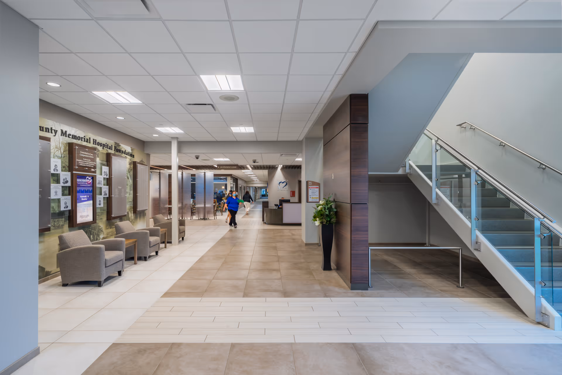 Hospital lobby interior with seating, information boards, and a right-side staircase.