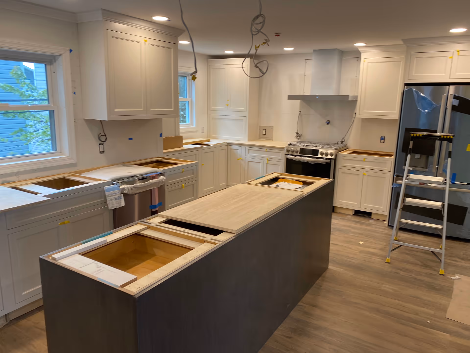 Kitchen under renovation with white cabinets, island, stainless appliances, and exposed wiring.