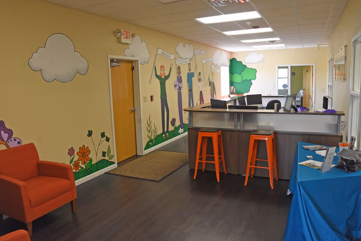 Colorful facility lobby with a reception desk, painted walls, orange stools, and seating area.