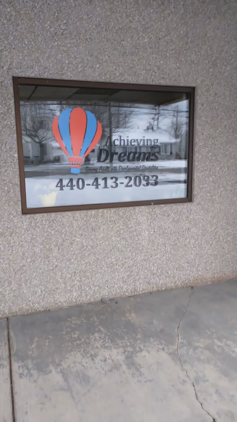 Exterior wall with a window sign reading Achieving Dreams and the phone number.