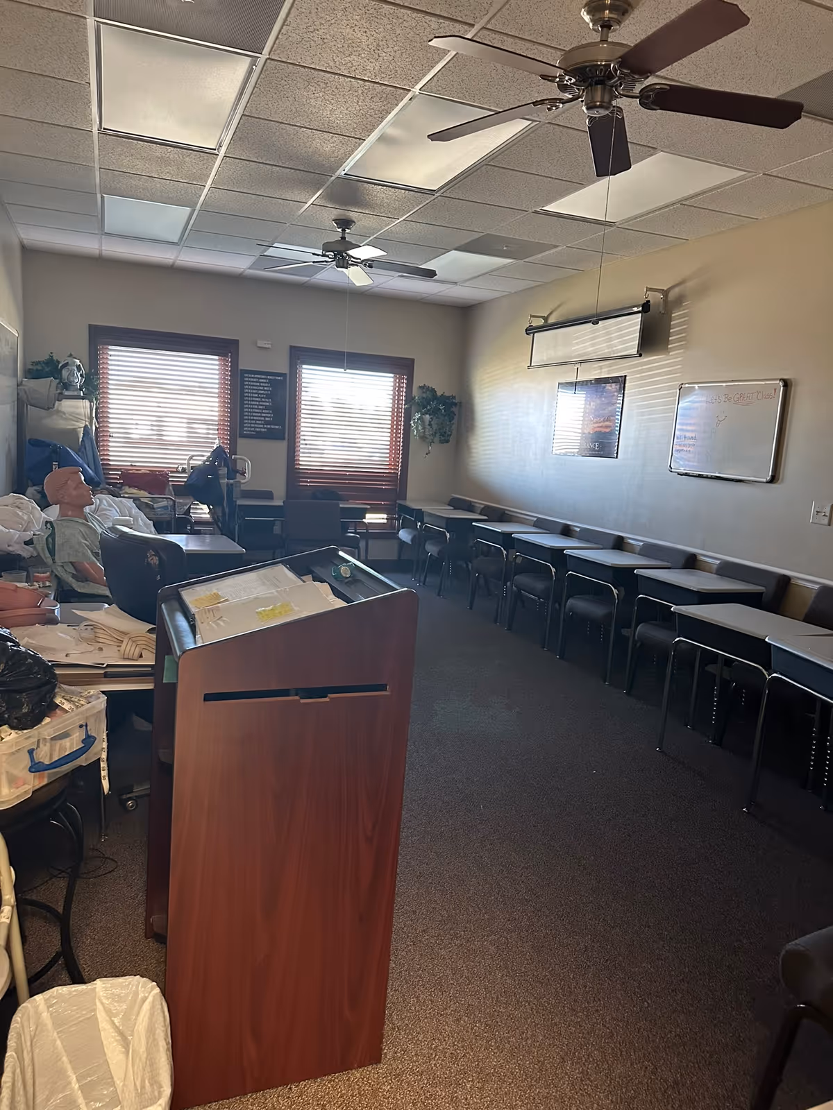 A care facility classroom with a podium, rows of desks, and ceiling fans.