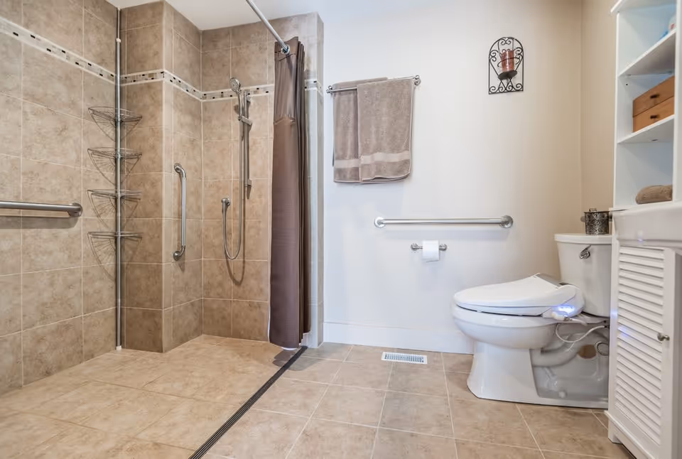 Accessible tiled bathroom with a walk-in shower, grab bars, toilet, and storage shelves.