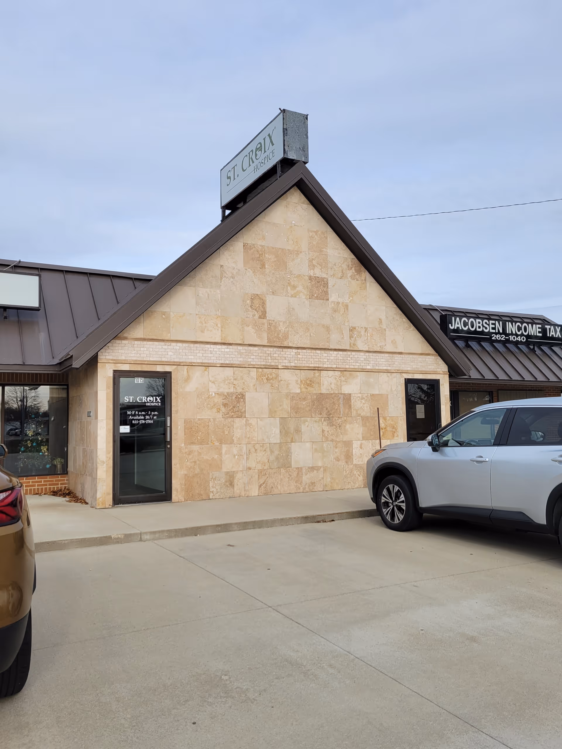 Front view of a stone hospice building with a St. Croix Hospice sign and parked cars.