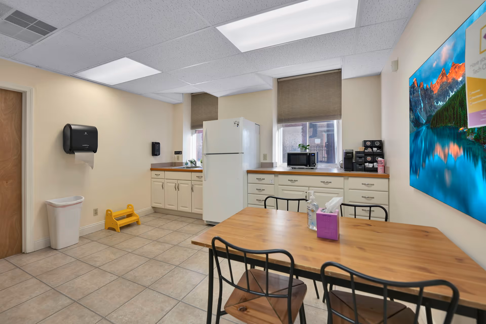 Interior kitchenette area in a senior living facility with table, chairs, fridge, microwave, and cabinets.