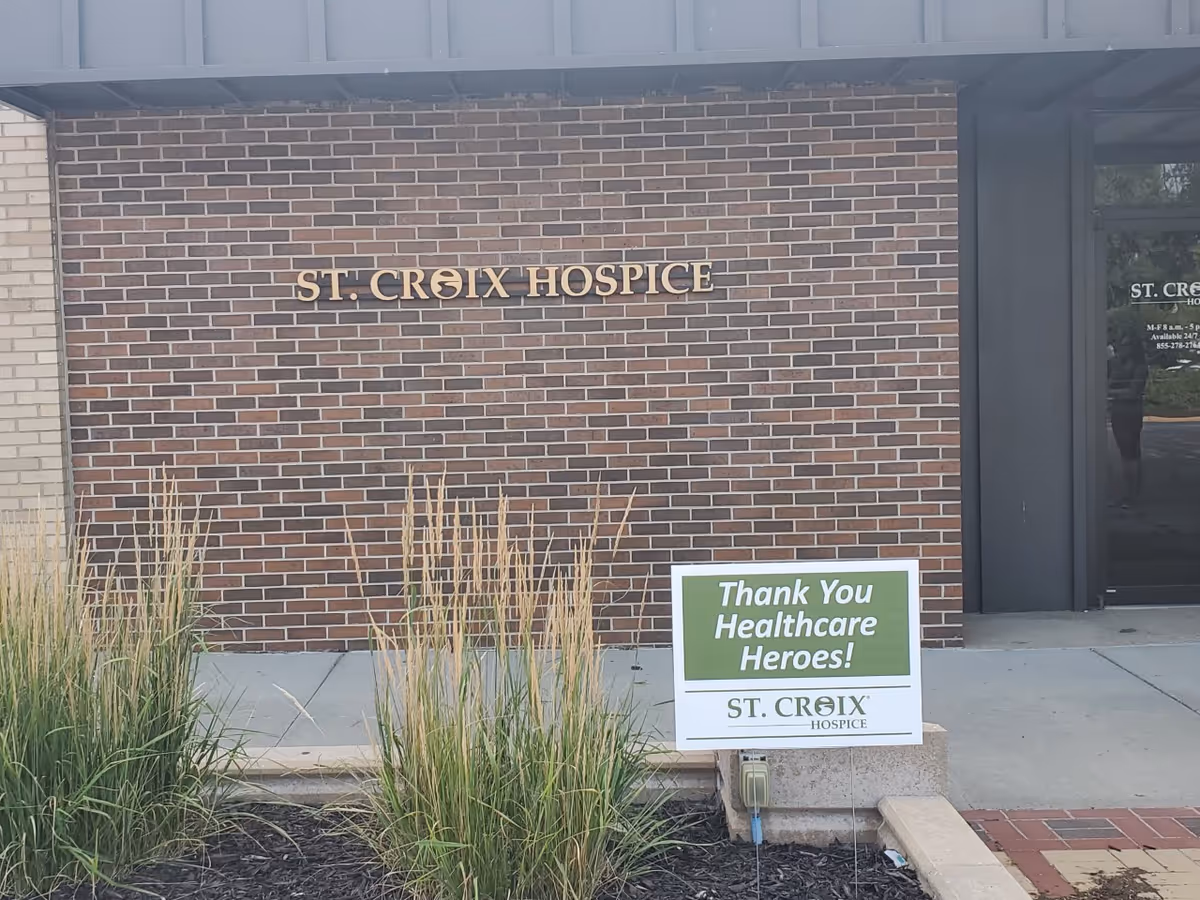 Brick exterior wall with St. Croix Hospice sign and a roadside thank-you healthcare heroes sign.