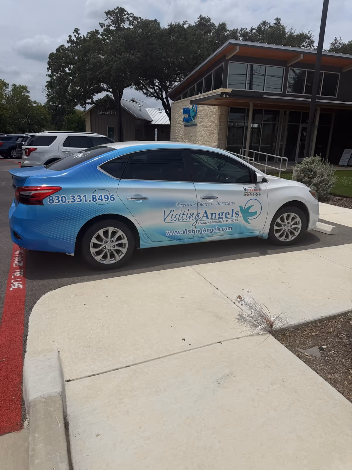 Blue and white Visiting Angels promotional car parked in front of a modern care facility.