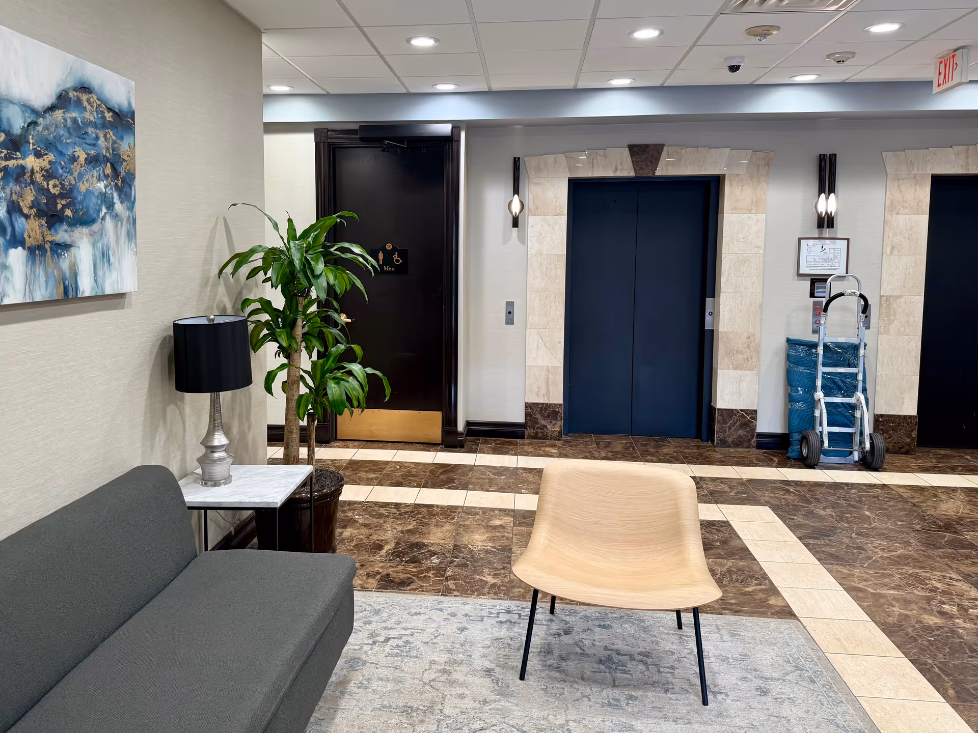 Lobby area in a senior living facility with seating, plant, art, and elevator doors.