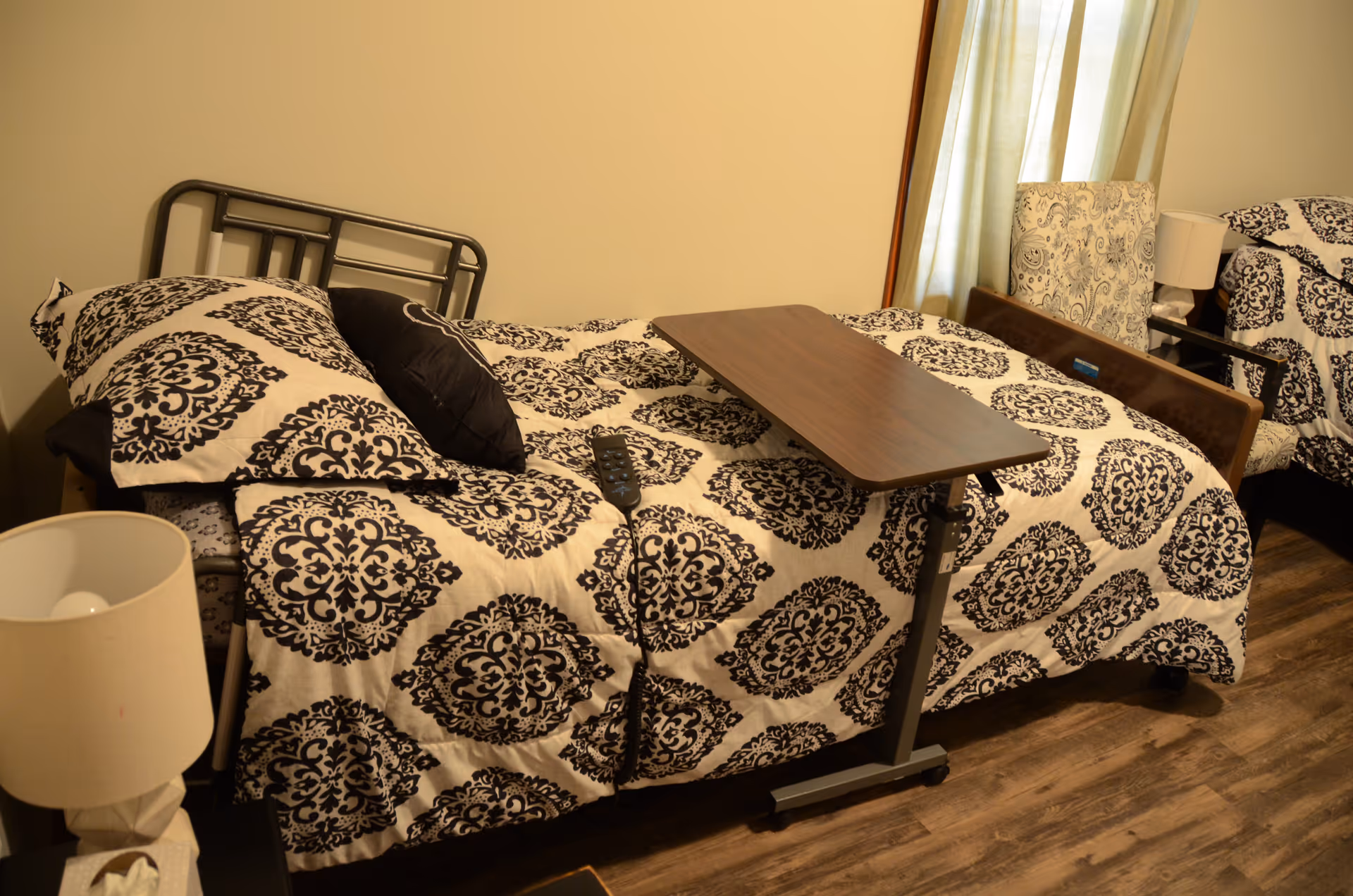 Two single beds with patterned bedspreads and a shared overbed table in a bedroom.