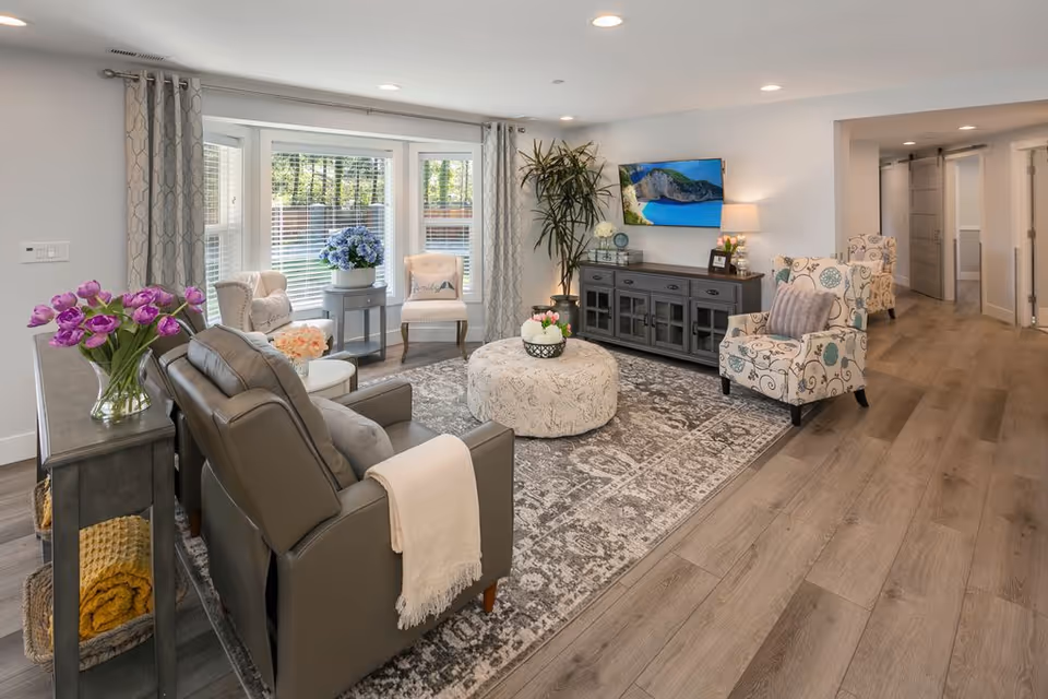 A bright, modern living room with sofa, chairs, rug, and TV in Ashford at Firdale Village.