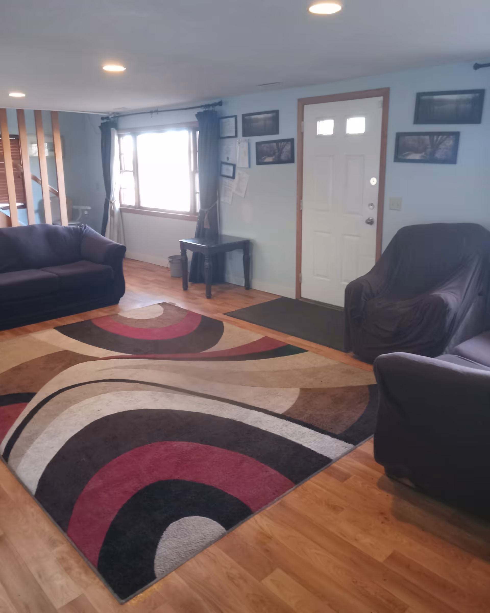 A cozy living room with sofas, chairs, a rug, and a door by a window.