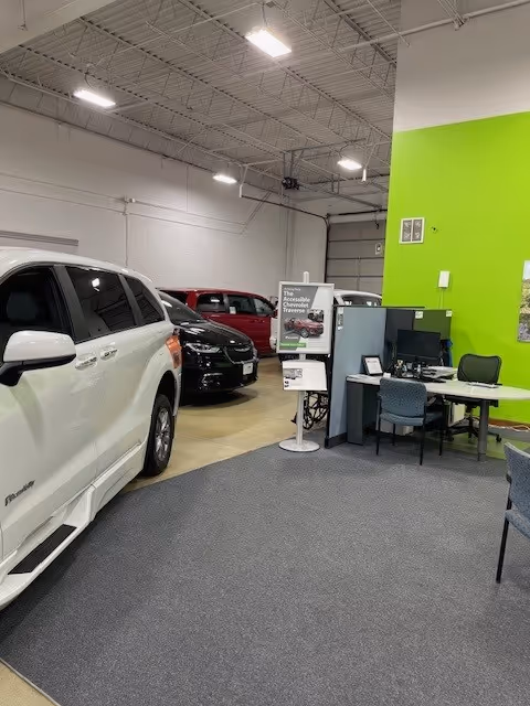 Indoor showroom with a white SUV, other cars, and a small office area.
