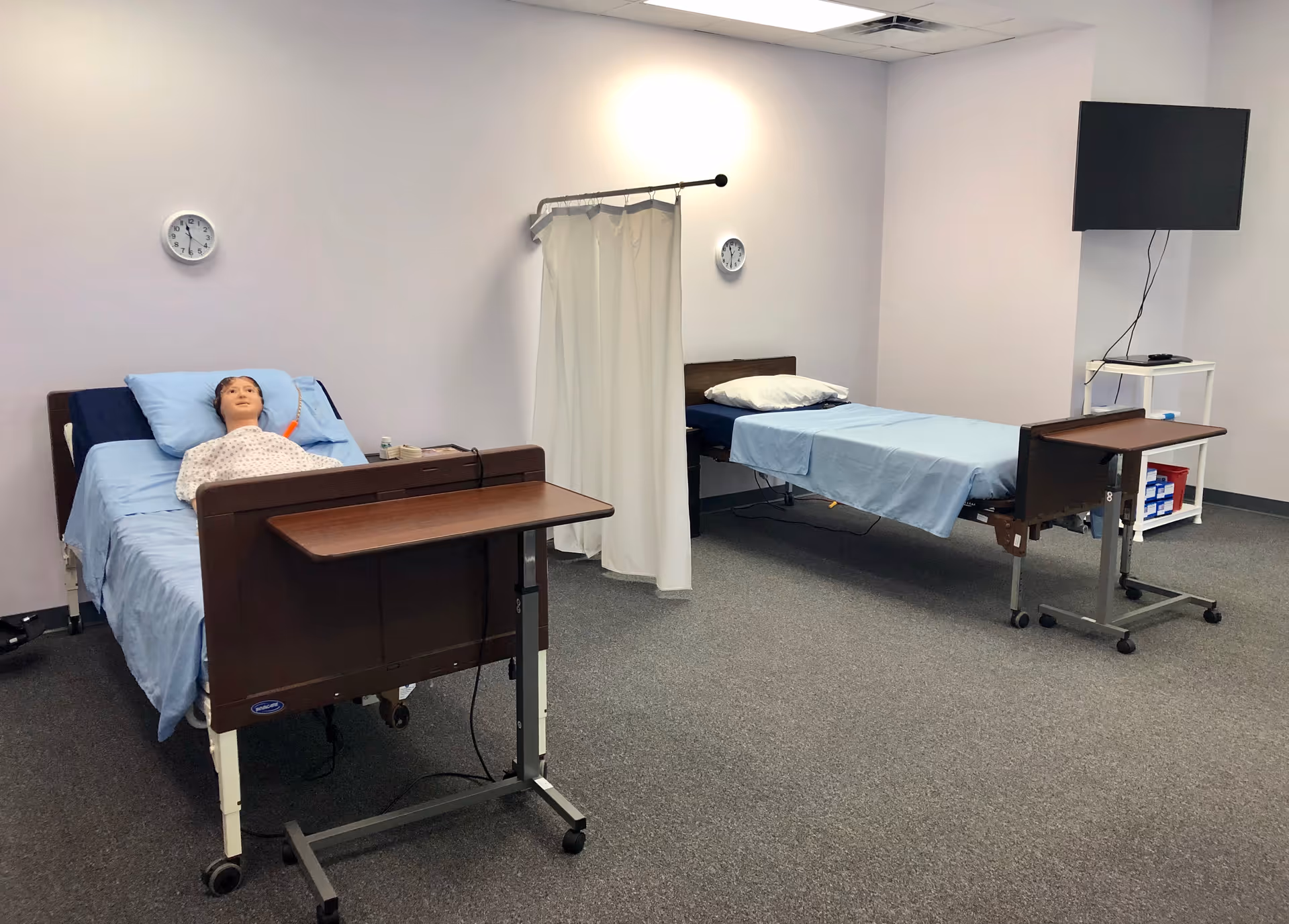 Two hospital beds in a CNA training room with a mannequin on the left bed.