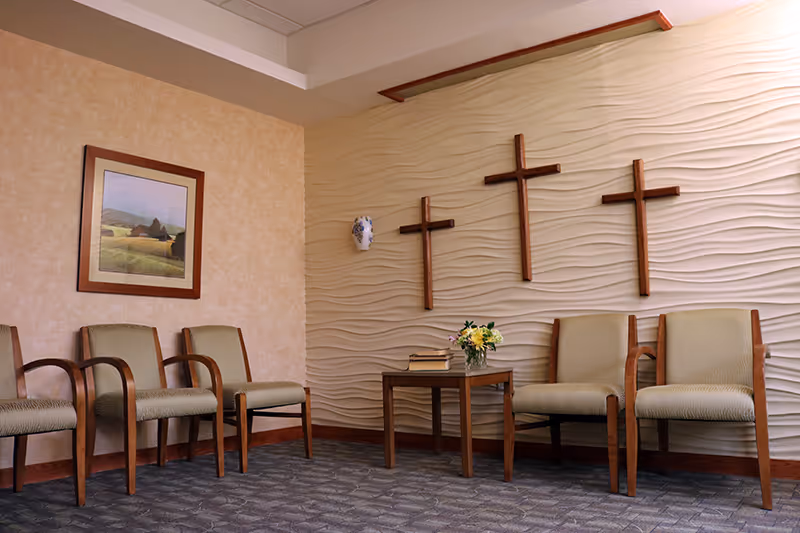 A quiet waiting area with beige chairs, a small table, and crosses on a textured wall.