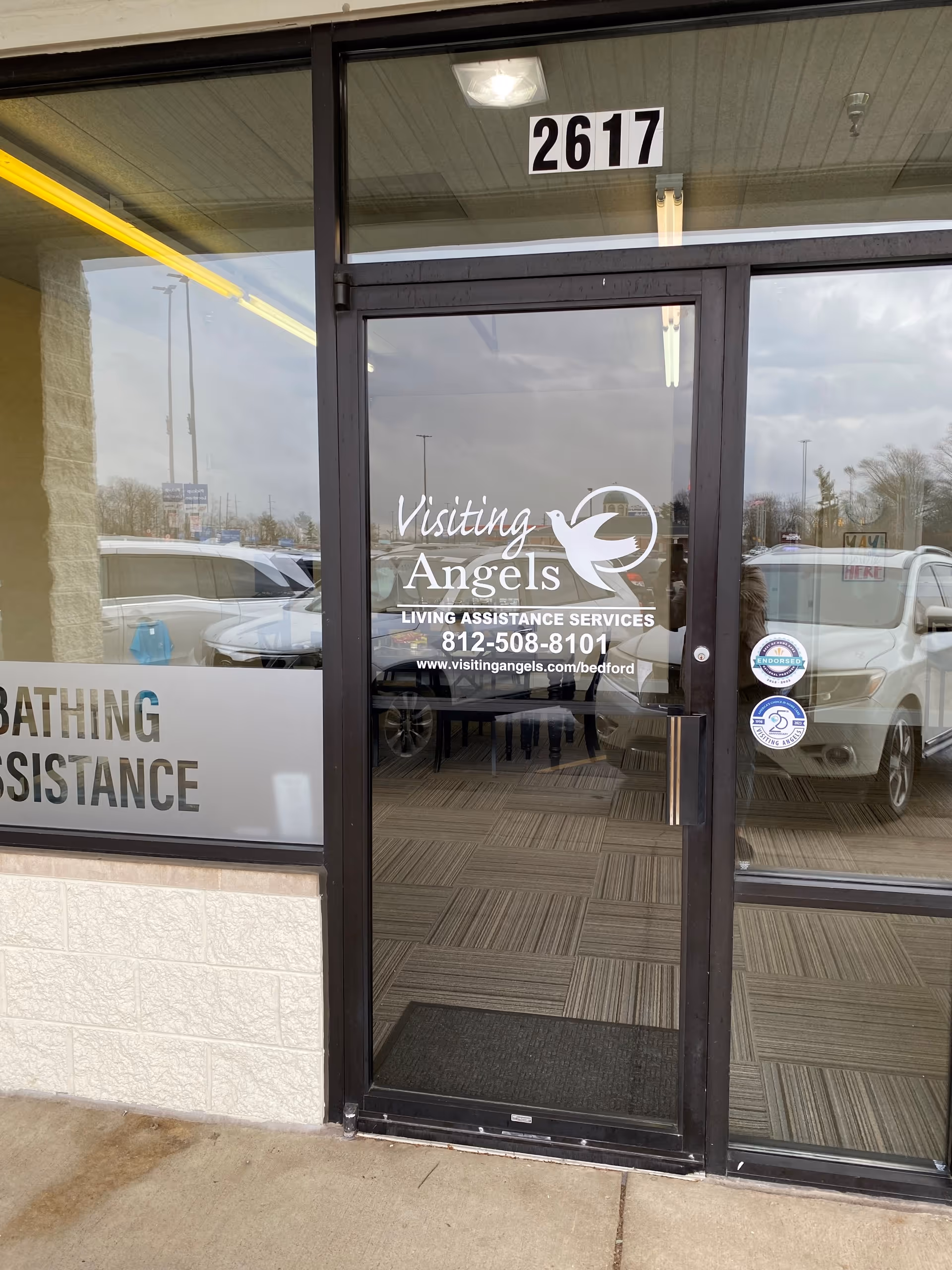 Glass entrance door displaying Visiting Angels logo with reflections of parked cars.