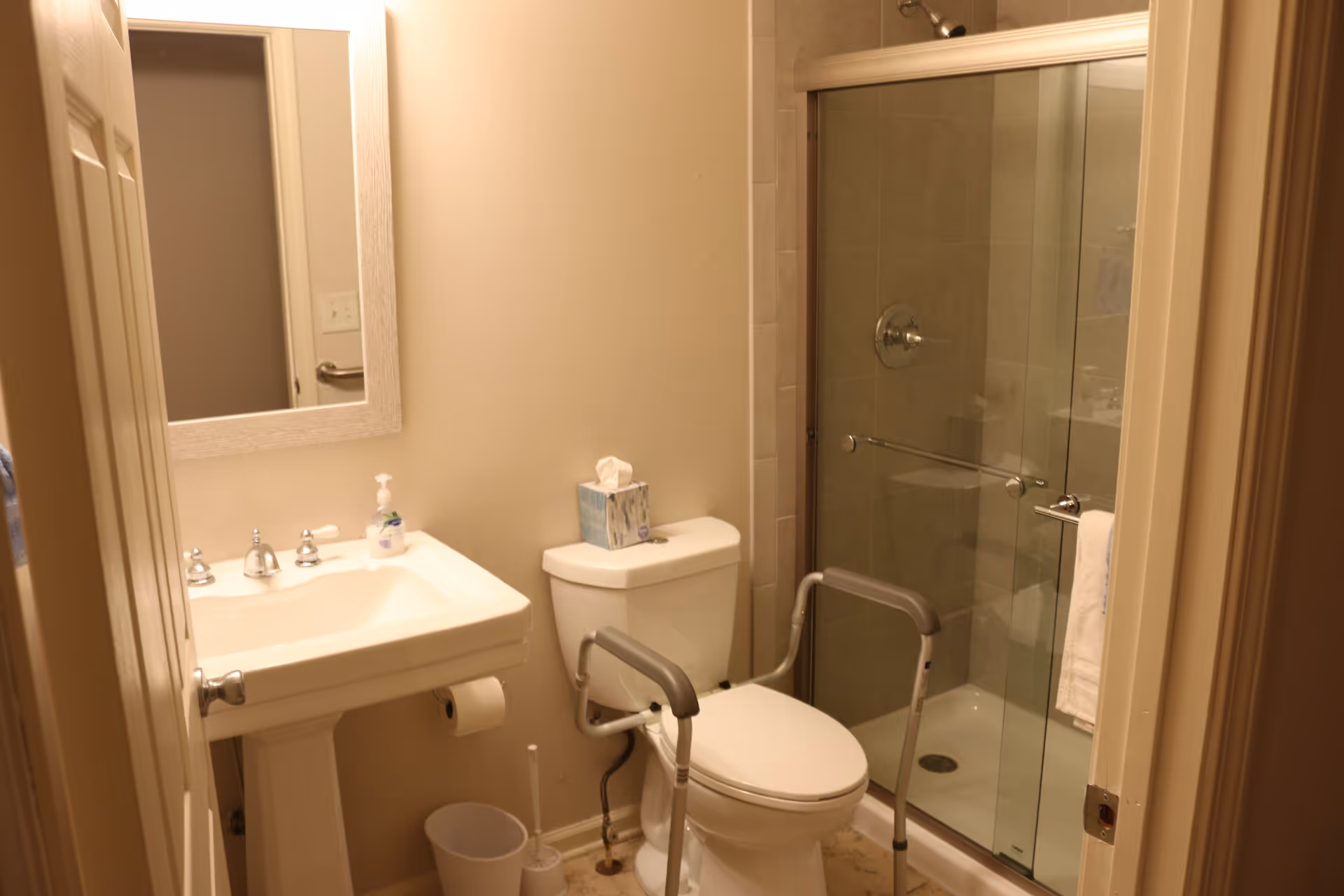Accessible bathroom with grab bars, toilet, sink, and glass-enclosed shower.