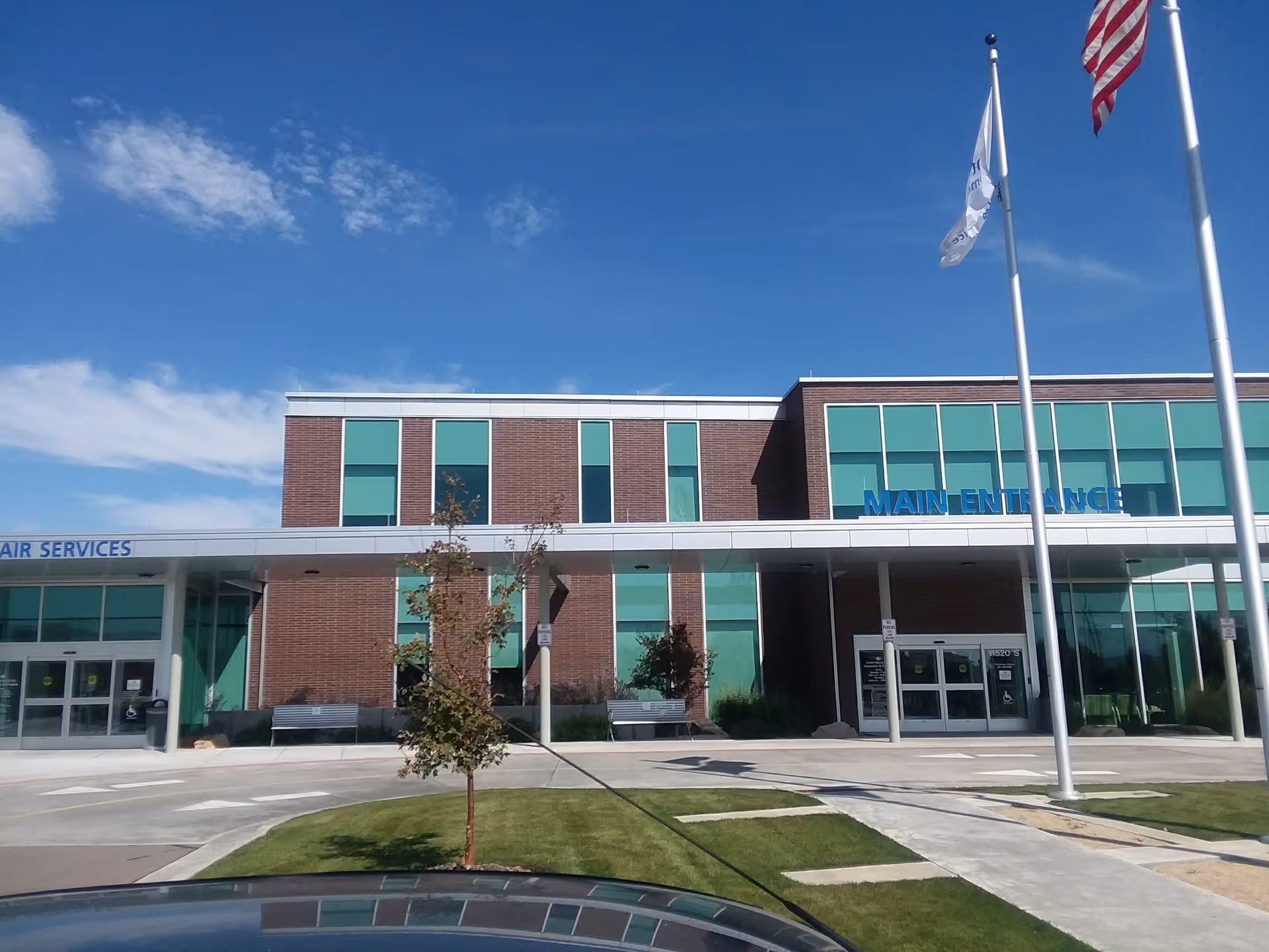 Brick-and-glass facility facade with a main entrance, flagpoles, and manicured landscaping.