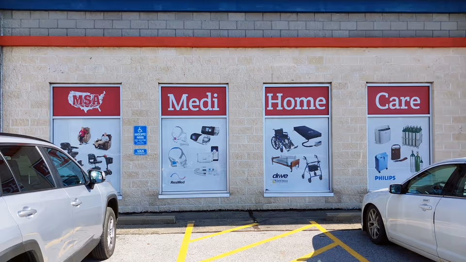 Exterior view of Medi Home Care storefront with four large windows and parked cars.