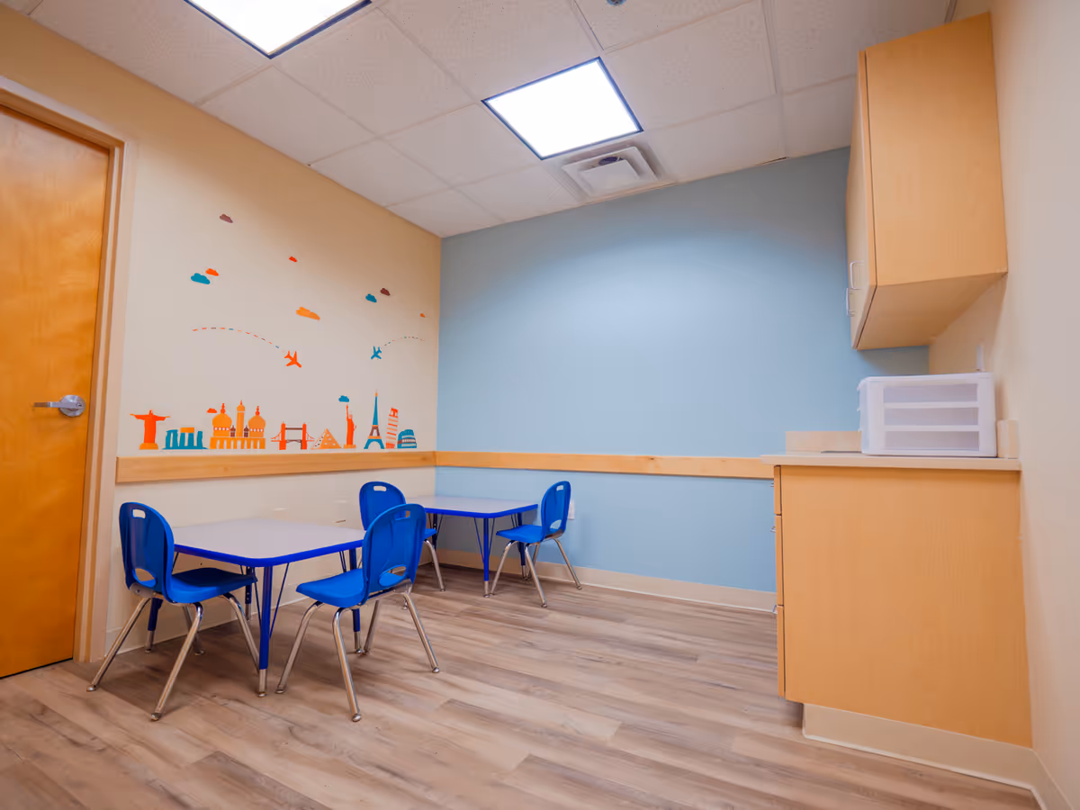 Bright, kid-friendly activity room with blue tables, chairs, and a wall mural.