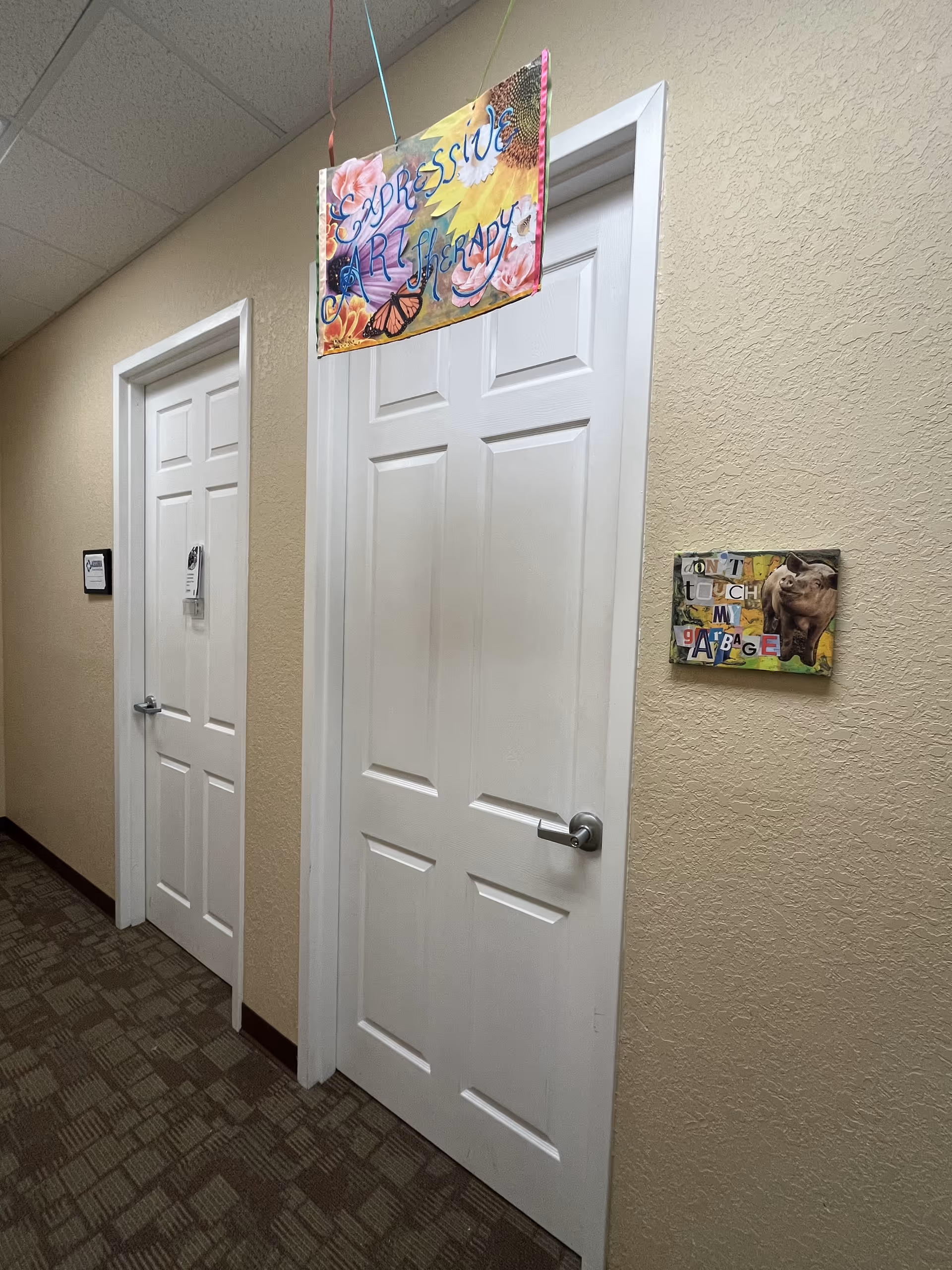 Interior hallway in a senior living facility with white doors, beige walls, and colorful signs.
