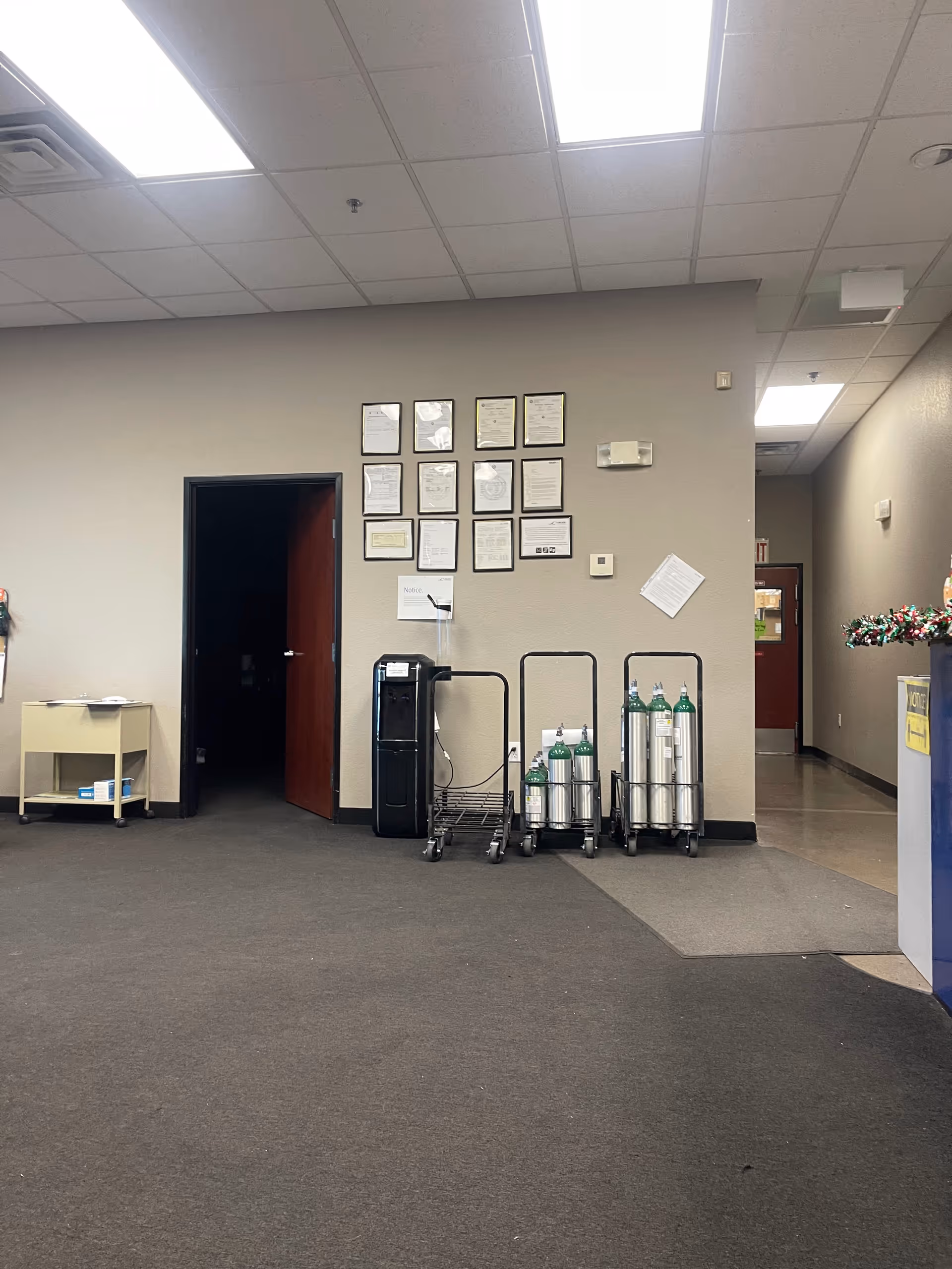 Interior facility hallway with oxygen cylinders on carts, wall certificates, and a water cooler.