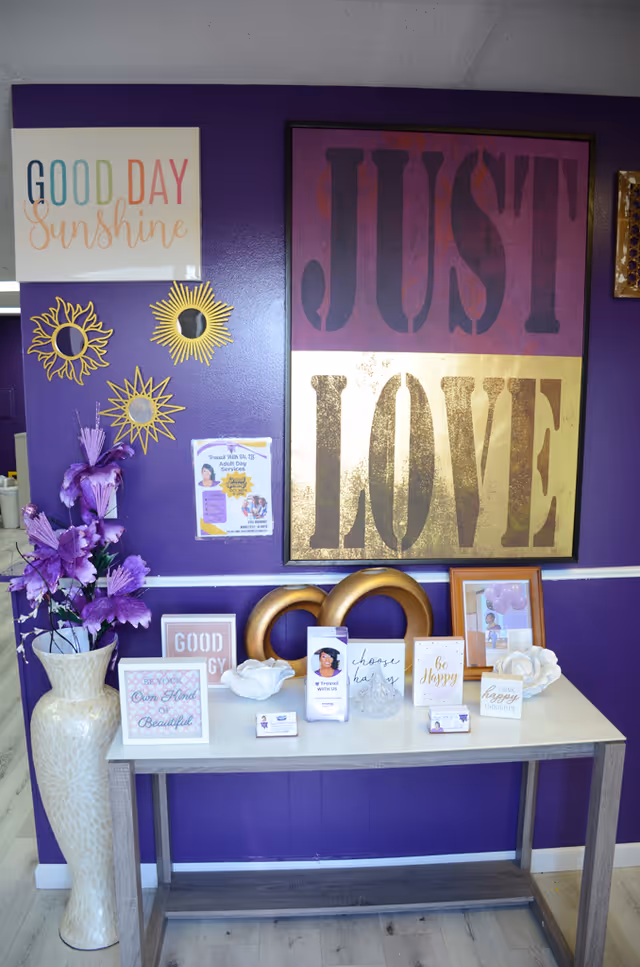 Purple interior with large JUST LOVE art above a table of decorative signs and sunburst decor.