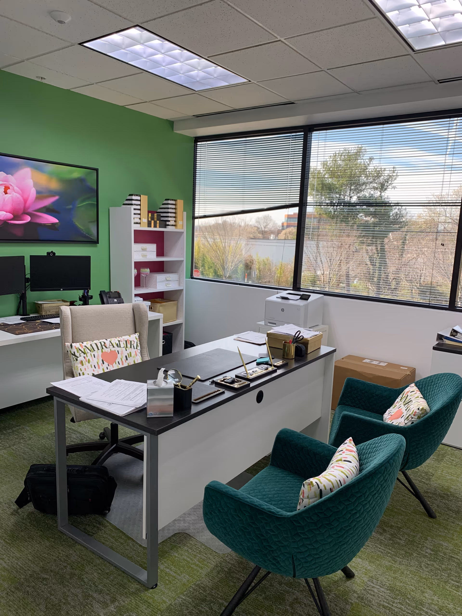 Modern office with green accent wall, desk, two teal chairs, and large window.
