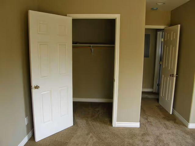 Open closet in a beige bedroom with carpet and two doorways.