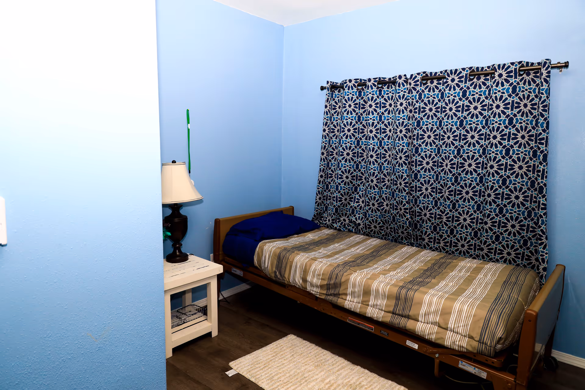 Blue bedroom with single bed, striped bedding, and patterned curtains.