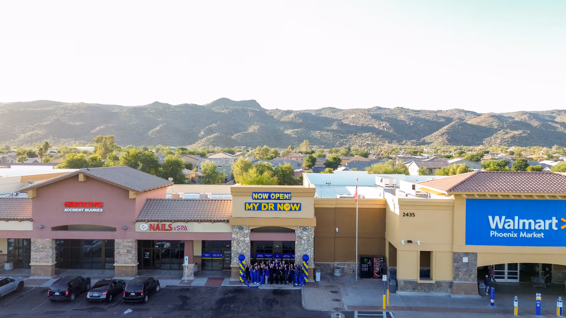 Strip mall storefronts including a My Dr Now grand opening sign and balloons.