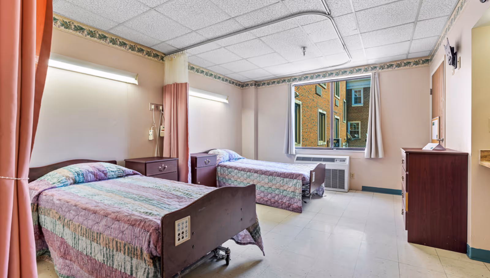 Two beds with pastel quilts in a shared senior living bedroom.