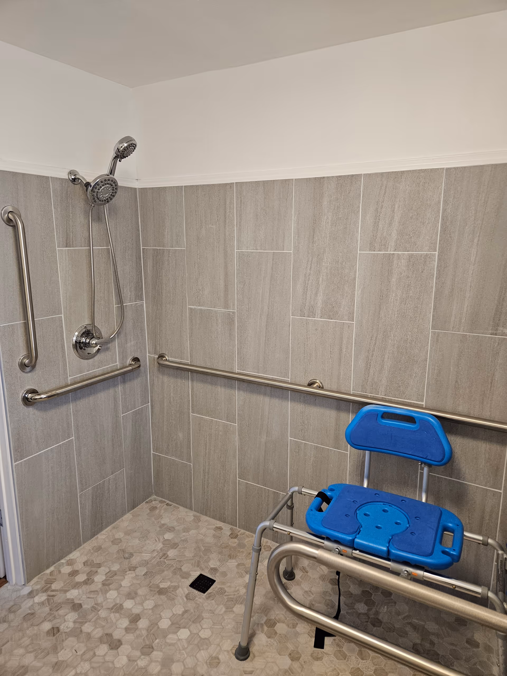 Accessible bathroom shower with grab bars and a blue shower chair.
